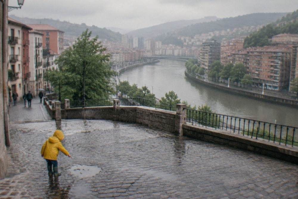 A toddler in a rain jacket pointing at puddles on a cobblestone square in Bilbao's old town