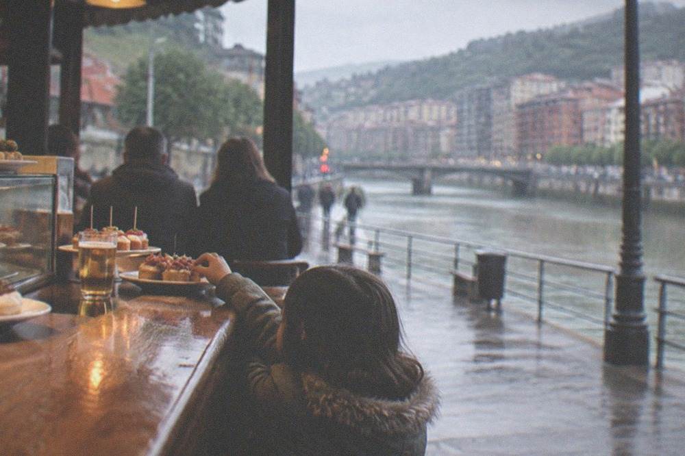 A child reaching for a small plate of food on a wooden bar counter in a pintxos bar