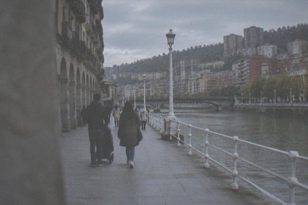 A family walking a stroller down a wide flat shopping street with arched buildings in Bilbao