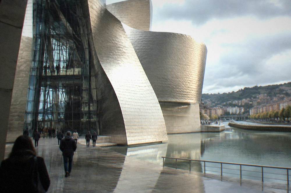 Visitors inside the tall glass and steel atrium of the Guggenheim Museum Bilbao on a grey day