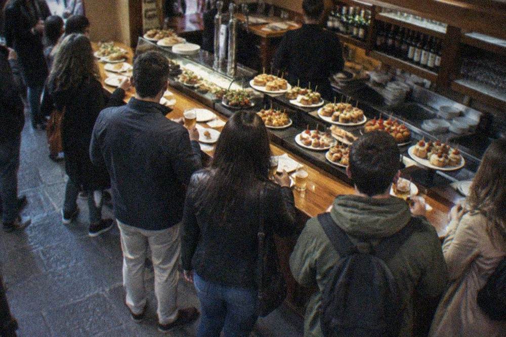 People standing at a busy pintxos bar counter in Bilbao's Old Town in the early evening