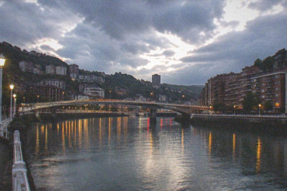 The Bilbao estuary at dusk with city lights reflecting on the water and bridges crossing the river